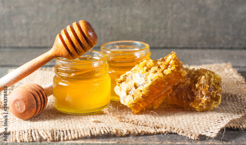 Honey dripping from a wooden honey dipper in a jar on wooden grey rustic background Honey dripping from a wooden honey dipper in a jar on wooden grey rustic background