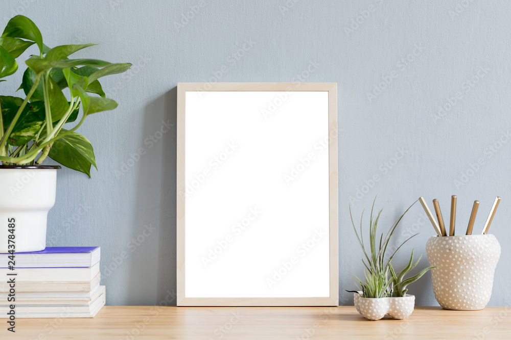 Minimalistic home interior with mock up photo frame on the brown wooden table with books, beautiful plant in stylish pot and tillandsia in design pots. Grey walls. Stylish decor of desk. Minimalistic home interior with mock up photo frame on the brown wooden table with books, beautiful plant in stylish pot and tillandsia in design pots. Grey walls. Stylish decor of desk.