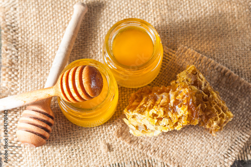 Honey dripping from a wooden honey dipper in a jar on wooden grey rustic background