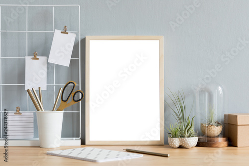 Home interior of creative desk with mock up photo frame on the brown wooden table with office accesories, tillandsia in design pots, notebook and notes. Grey walls. Minimal concept of mockup.