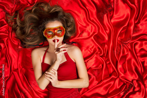 Woman in Venetian Mask Lying on Red Silk Fabric Background, Fashion Model Carnival Secret, Finger on Lips