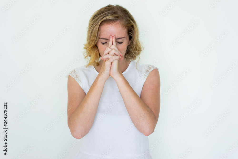 Young pretty woman touching forehead with her hands clasped. Lady standing with closed eyes and thinking hard. Contemplation concept. Isolated front view on white background. Young pretty woman touching forehead with her hands clasped. Lady standing with closed eyes and thinking hard. Contemplation concept. Isolated front view on white background.