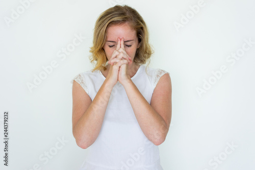 Young pretty woman touching forehead with her hands clasped. Lady standing with closed eyes and thinking hard. Contemplation concept. Isolated front view on white background.