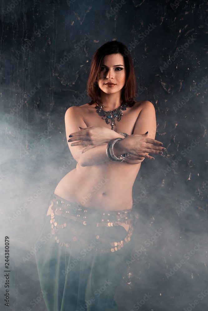 Obraz premium Sexy women performs belly dance in ethnic dress on dark smoky background