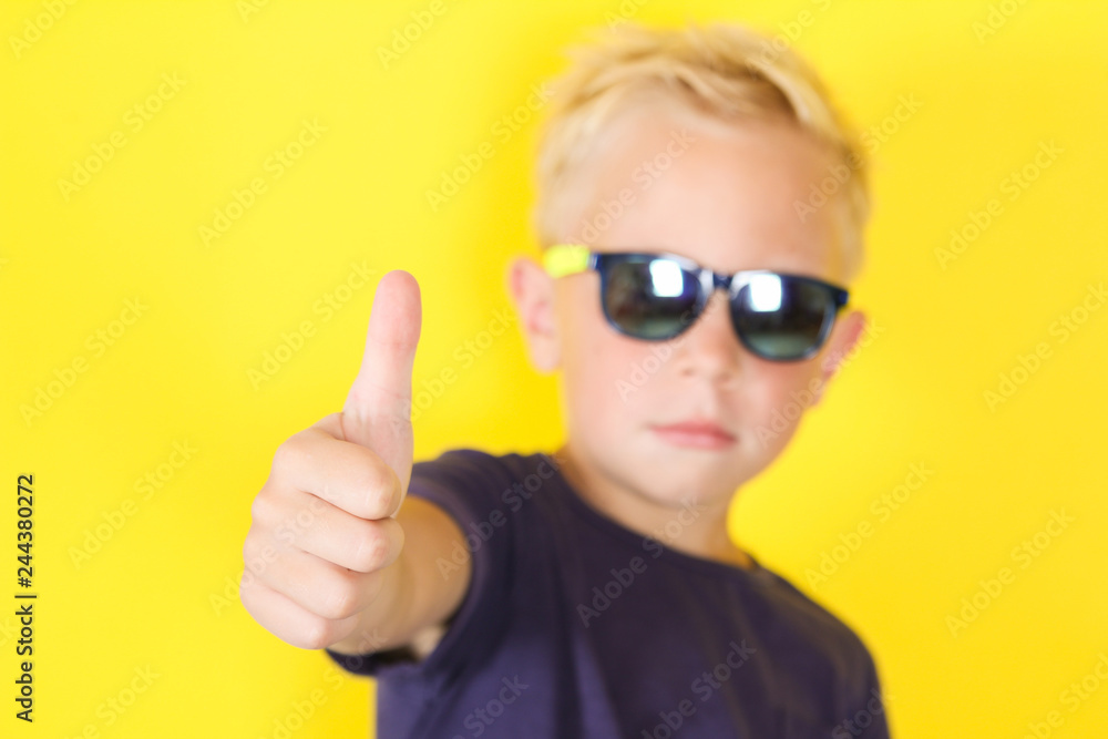Cute blond boy wearing sunglasses showing Thumbs Up