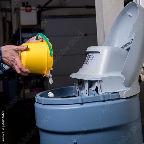 Φωτογραφία Yellow bucket pours salt pellets by a man into a water softener