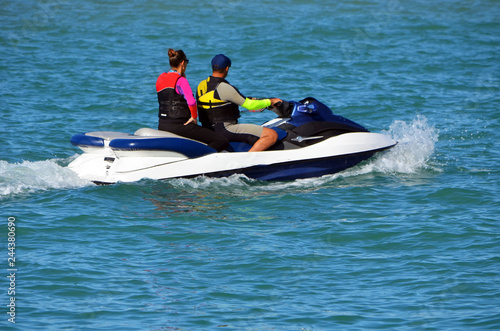 Man and a woman riding tandem of a blue and white jet ski