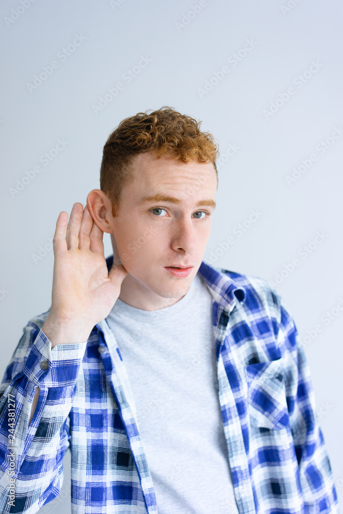 Curious young man holding hand near ear. Attractive guy looking at camera. News concept. Isolated front view on white background. Curious young man holding hand near ear. Attractive guy looking at camera. News concept. Isolated front view on white background.