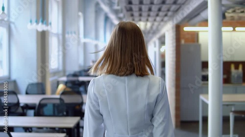 back view woman doctor wearing white lab coat walking in open space office. slow motion