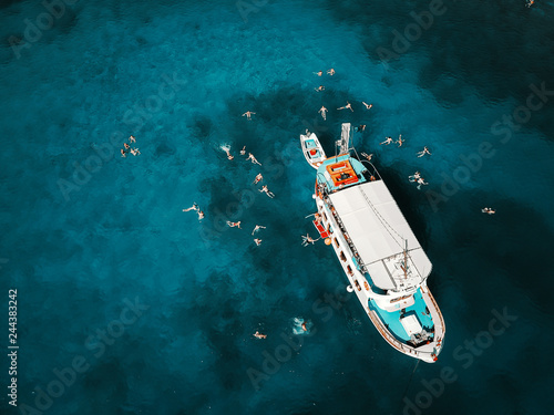 Aerial shot of beautiful blue lagoon at hot summer day with sailing boat. Top view of people swimming around the boat. © dusanpetkovic1