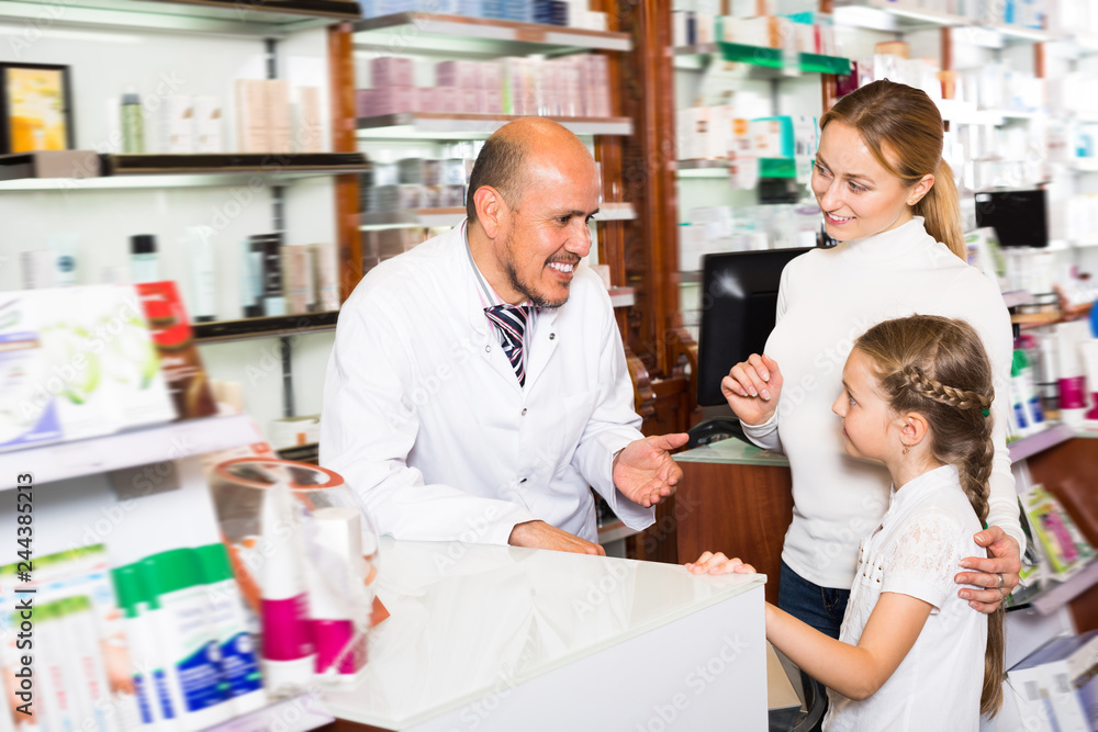 Smiling adult male pharmacist helping customers