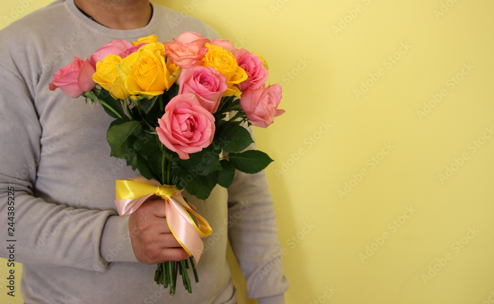 a man with pink and yellow roses in the hands on yellow background. valentine day love beautiful. Copyspace for text.