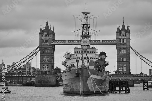 Desaturized or black and white picture of british light cruiser ship HMS Belfast in front of Tower bridge in London, capitol of United Kingdom on the Thames river, used like museum war ship. photo