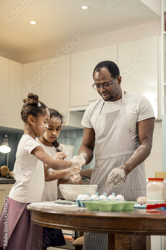 Father wearing striped apron feeling amazing cooking with daughters