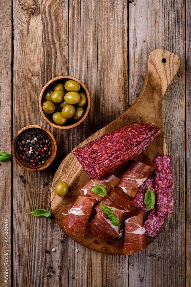 prosciutto, salami and olives on wooden  background, top view