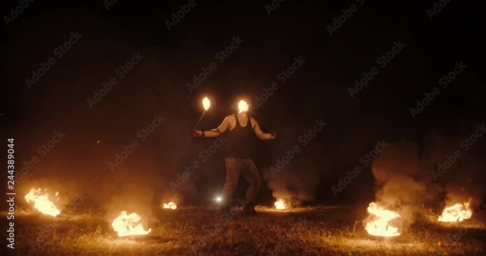 Cool male fire show stuntsman performing, flailing his burning sticks, standing in circle of burning bowls- slow motion 4k Cool male fire show stuntsman performing, flailing his burning sticks, standing in circle of burning bowls- slow motion 4k