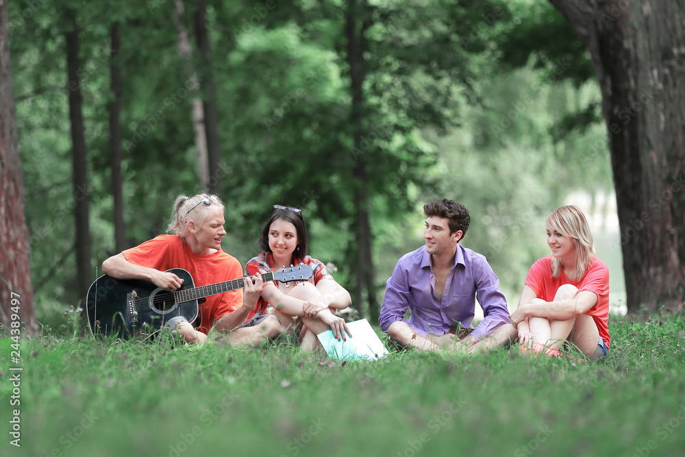group of students sing songs sitting on the lawn in the city Park group of students sing songs sitting on the lawn in the city Park