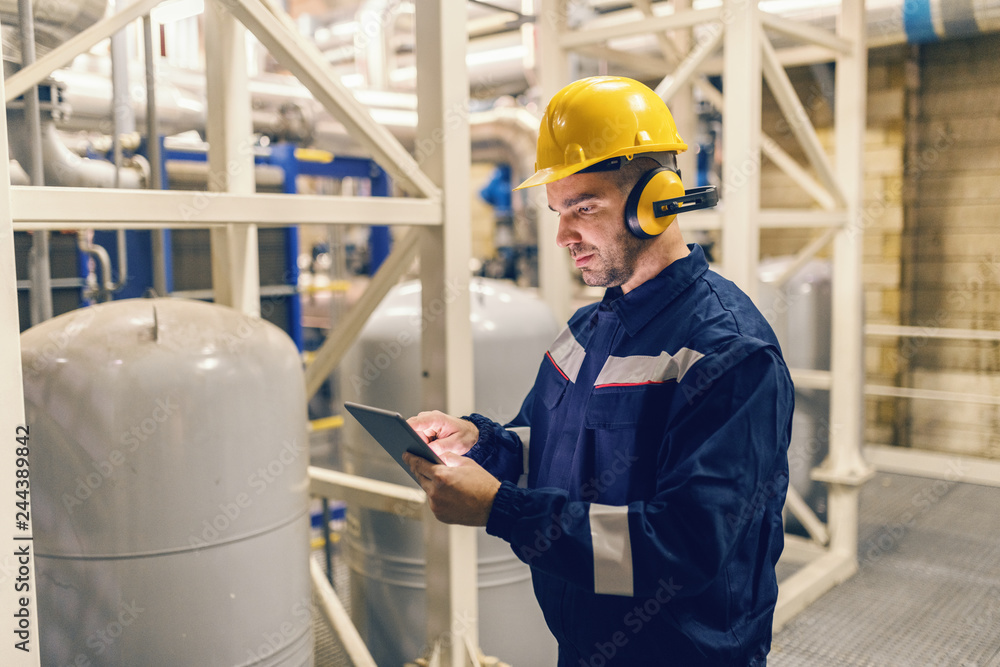 © Dusan Petkovic - Young Caucasian man in protective suit using tablet while standing in heating plant. © Dusan Petkovic - Young Caucasian man in protective suit using tablet while standing in heating plant.