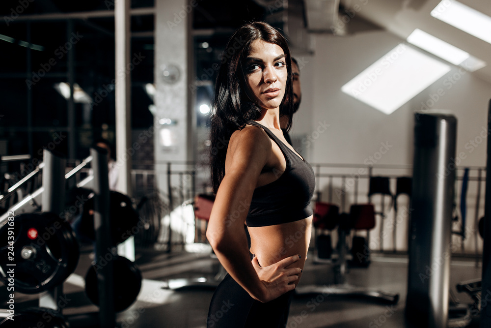 Slim dark-haired girl dressed in black sport clothes is doing warm up in the gym