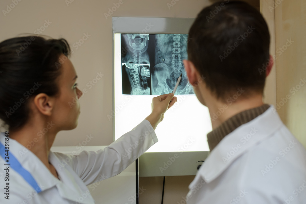 Back view: picture of two doctors exploring spinal x-ray: lumbar and cervical region - first 2 cervical vertebrae (axis and atlas), coxofemural joint Back view: picture of two doctors exploring spinal x-ray: lumbar and cervical region - first 2 cervical vertebrae (axis and atlas), coxofemural joint