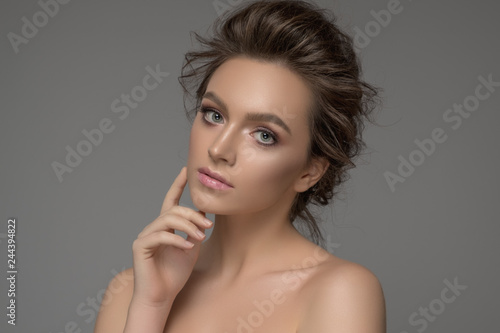 Beauty portrait of model with trendy make-up. Fashion shiny highlighter on skin, sexy gloss lips make-up. Photo of girl with perfect skin on grey background. Beauty & Skin care concept