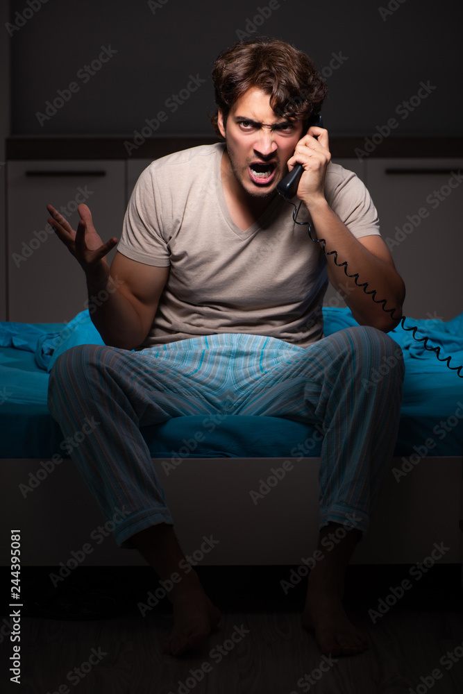 Fototapeta premium Young man talking on phone in bed