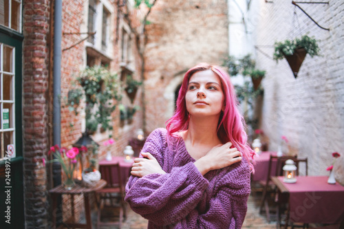 A young, beautiful girl with pink hair walks through the old stone yard. © Aleksei Zakharov