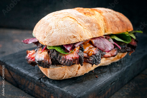 Traditional barbecue pulled pork piece of Bosten butt as sandwich with lettuce as closeup on a black board photo