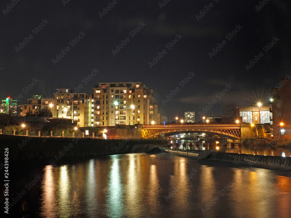 the river aire in leeds at night showing buildings on both sides of crown point bridge and the weir with bright lights reflected in the water