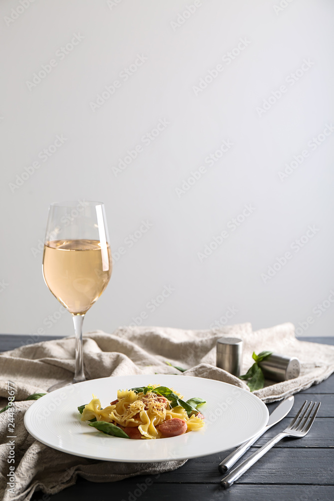 Glass of tasty wine and plate with macaroni and sausages on table