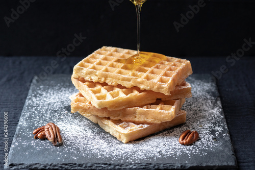sweet tasty Belgian waffles close-up, sprinkled with powdered sugar, pecans, topped with honey