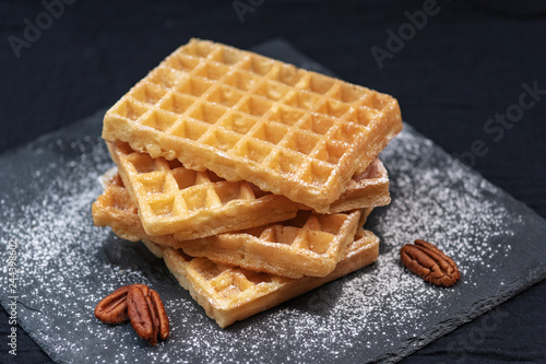 sweet tasty Belgian waffles close-up, sprinkled with powdered sugar, pecans,