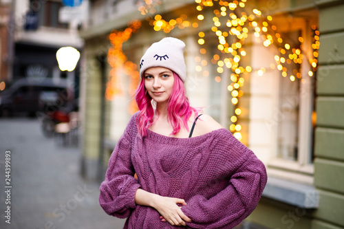 portrait of beautiful young girl with pink hair and purple sweater on city lights background.
