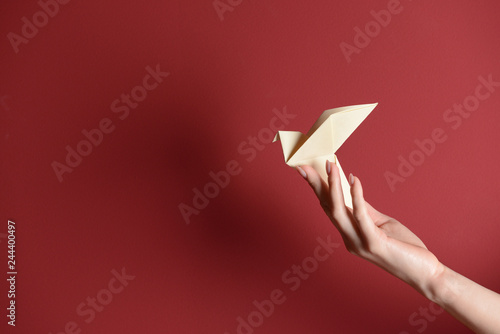 Female hand with origami bird on color background photo