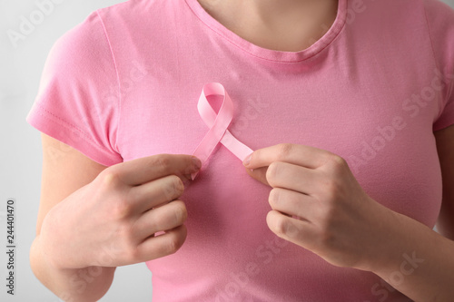 Woman with pink ribbon on light background  closeup. Breast cancer awareness concept