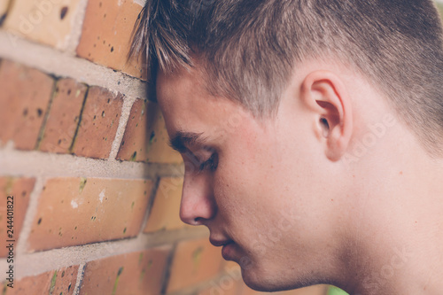 Canvas Print Side view of a sad young man leaning his head against the brick wall