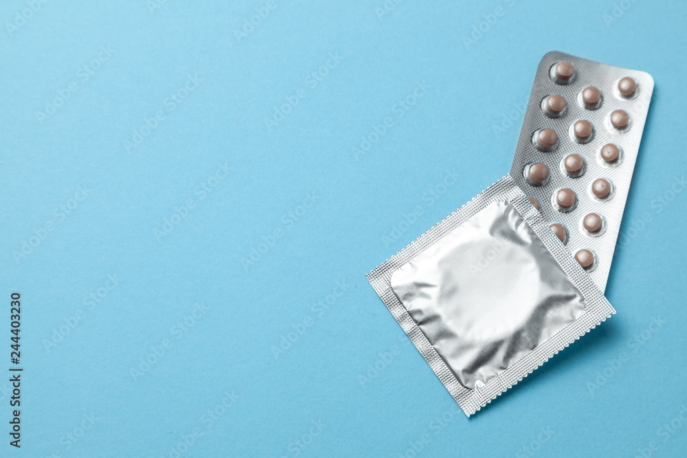 Birth control pills and condom in package on blue background. The concept of choosing method of contraception, birth control pills or condom. Copy space for text Birth control pills and condom in package on blue background. The concept of choosing method of contraception, birth control pills or condom. Copy space for text