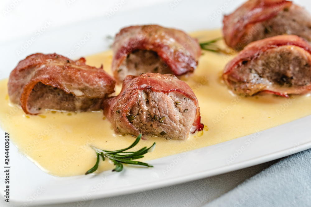 Baked pork tenderloin wrapped in bacon served in a cheese sauce with rosemary Baked pork tenderloin wrapped in bacon served in a cheese sauce with rosemary