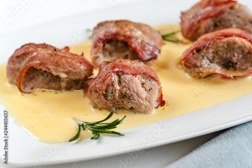 Baked pork tenderloin wrapped in bacon served in a cheese sauce with rosemary