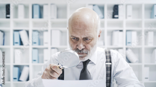 Billede på lærred Corporate businessman checking paperwork with a magnifier