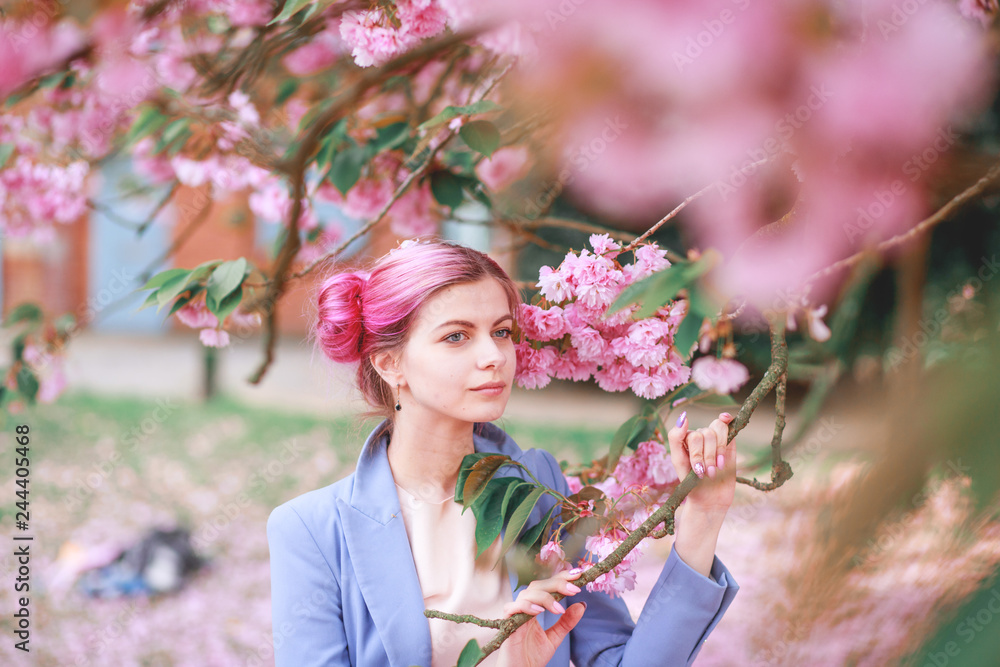 Obraz premium Beautiful girl with pink hair in a fashionable blue pantsuit standing next to colorful flowers.