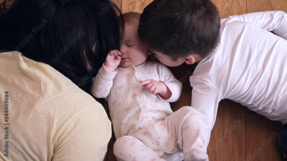 Top view happy family mother with kid son kiss little baby sister lying on floor Top view happy family mother with kid son kiss little baby sister lying on floor