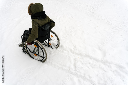 Disabled handicapped man has a hope. He sits in a wheelchair and looks at a mountain of snow. The complexity of the movement of the disabled. On a wheelchair in the winter.