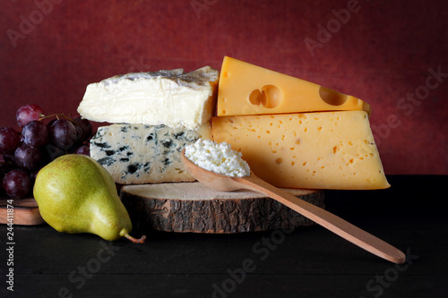 Cheese, grapes and pear on a wooden stand. Different types of cheese and fruit on a dark background. Camembert, blue cheese and cottage cheese. Dairy products and a bunch of grapes photo