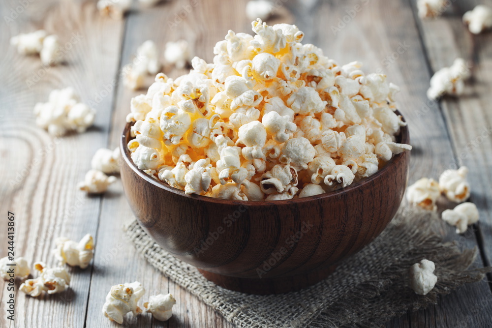 A wooden bowl of salted popcorn at the old wooden table. Dark background. selective focus A wooden bowl of salted popcorn at the old wooden table. Dark background. selective focus