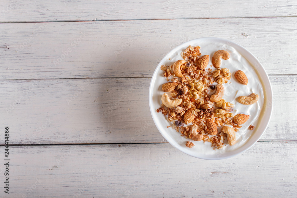 White plate with greek yogurt, granola, almond, cashew, walnuts on white wooden background. White plate with greek yogurt, granola, almond, cashew, walnuts on white wooden background.