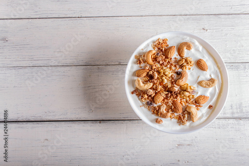 White plate with greek yogurt, granola, almond, cashew, walnuts  on white wooden background.