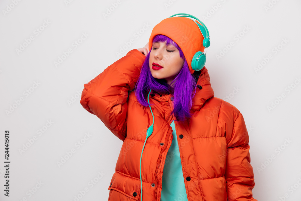 Portrait of a beautiful girl with purple hair in orange hat and jacket and with headphones on white background. Trendy style Portrait of a beautiful girl with purple hair in orange hat and jacket and with headphones on white background. Trendy style