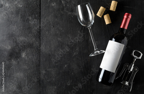 Red wine bottle with corkscrew, corks and wine glass on dark wooden table flat lay from above
