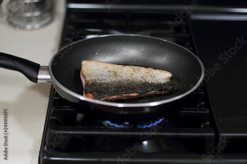 Wild caught Coho salmon frying in a pan with the skin side up.